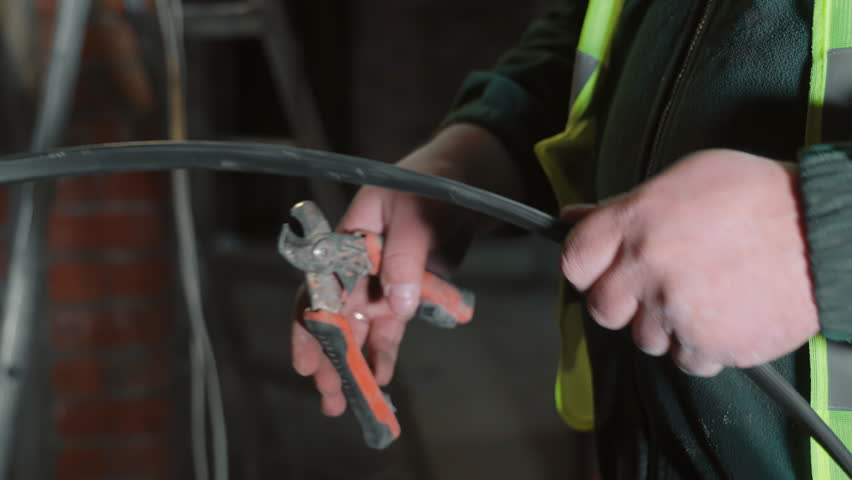 Close-up of hands cutting electrical cable with tool, Worker using a tool to cut a thick electrical cable