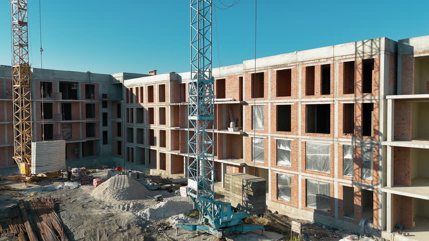 Construction crane and unfinished brick building on sunny day, A crane operating near a multi-story brick building under construction