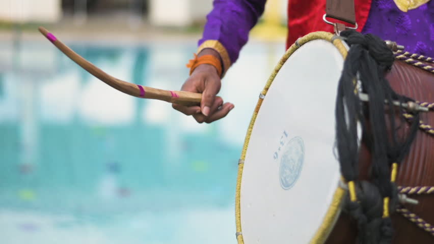Closeup view of an Indian man playing dhol at a wedding event. Slow motion view.