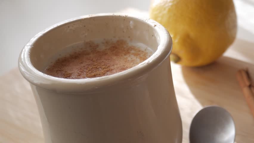 A warm cup of rice pudding topped with cinnamon, lemon, and a spoon by its side