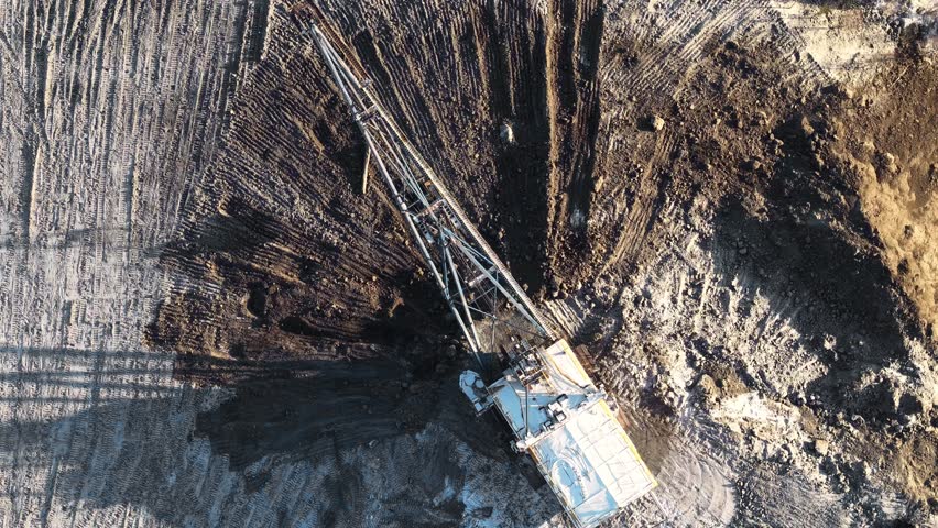 Aerial view of excavator digging in open pit coal mine revealing layers of earth and minerals, mining industry.