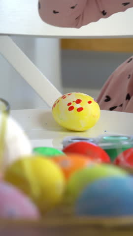 Mother and daughter painting Easter eggs together at home. Bright festive decorations, joyful atmosphere, creativity, and bonding. Colorful paints, bunny ears, and spring mood.