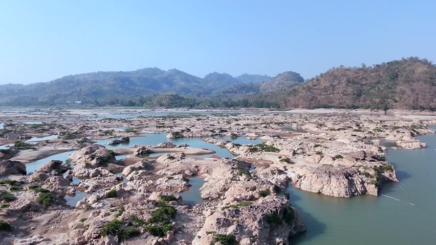 view of a rocky riverbed with scattered pools of water during the dry season, surrounded by mountains and sparse vegetation. The unique landscape highlights the effects of seasonal water levels