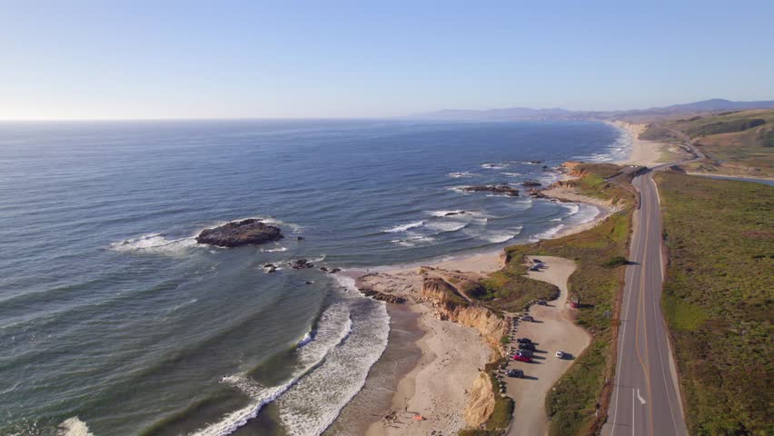 Aerial Drone Flyover of Beach on California coast with cars driving on the Pacific Coast Highway (PCH) at sunset