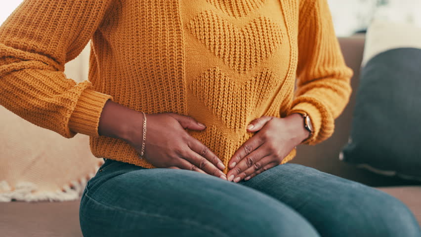 Woman, hands or stomach with pain for digestion, menstrual cycle or period cramps on sofa at home. Closeup, female person or belly ache with tummy bug, constipation or gastro reflux on couch at house