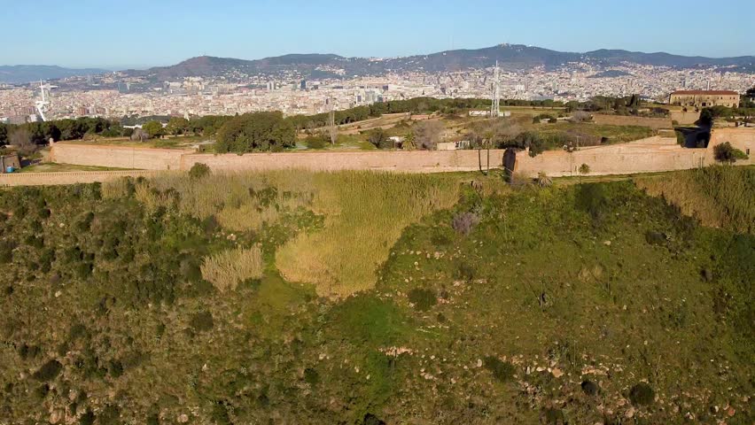 Scenic aerial view of Castle Hill of Montjuic with the city landscape of Barcelona in the background. Cinematic shot with blue sky, tourism and travelling in Spain