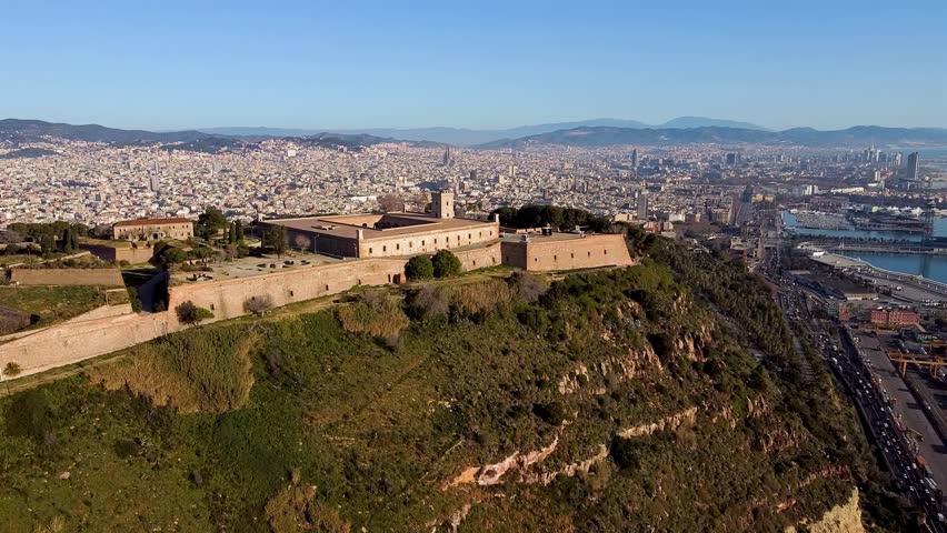 Scenic aerial view of Castle Hill of Montjuic with the city landscape of Barcelona in the background. Cinematic shot with blue sky, tourism and travelling in Spain