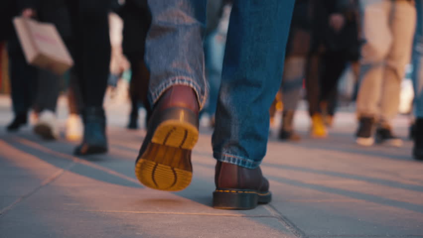 Back view close-up following male feet steps walking pedestrian crossing street on sunny autumn day. Man wearing leather boots goes crossroad. Low angle people crowd legs stepping, warm sunlight