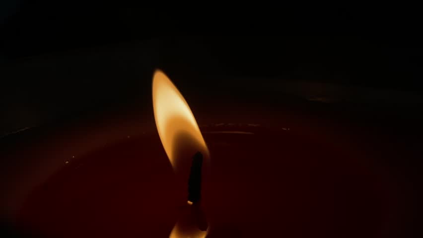A closeup video of a candle flickering in the dark