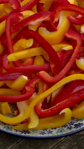 Sliced fresh yellow and red peppers on a plate. Table spin. Vertical video.