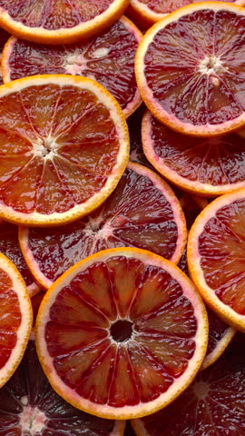 Unpeeled, sliced Sicilian oranges background. Table spin. Vertical video.