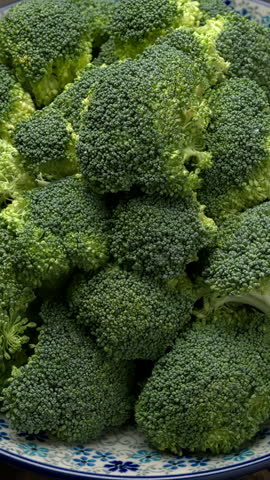 Plate of fresh green broccoli florets. Table spin, vertical video.