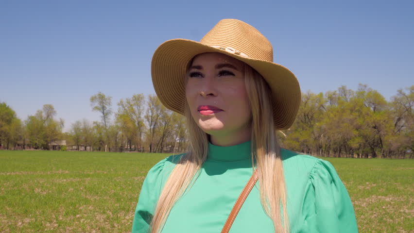 Young Woman in a Straw Hat Smiling in a Spring Field in green dress bright sun