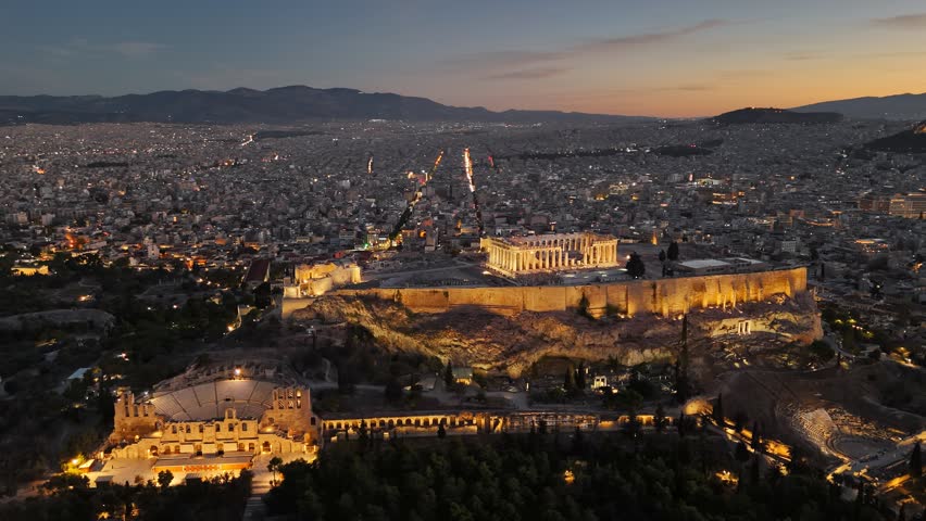 Aerial view of Parthenon in Athens, Greece before sunrise. Acropolis is illuminated with city lights, ancient theater sitting below. Fly over Parthenon in Athens - famous Greek tourist attraction