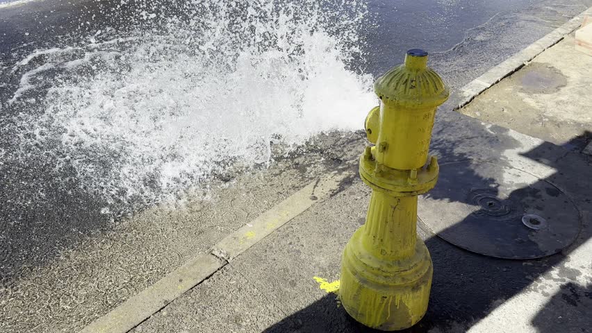 Yellow Fire Hydrant Spraying Water onto City Sidewalk