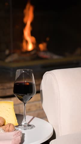 Glass of red wine and cheese in front of fireplace at home