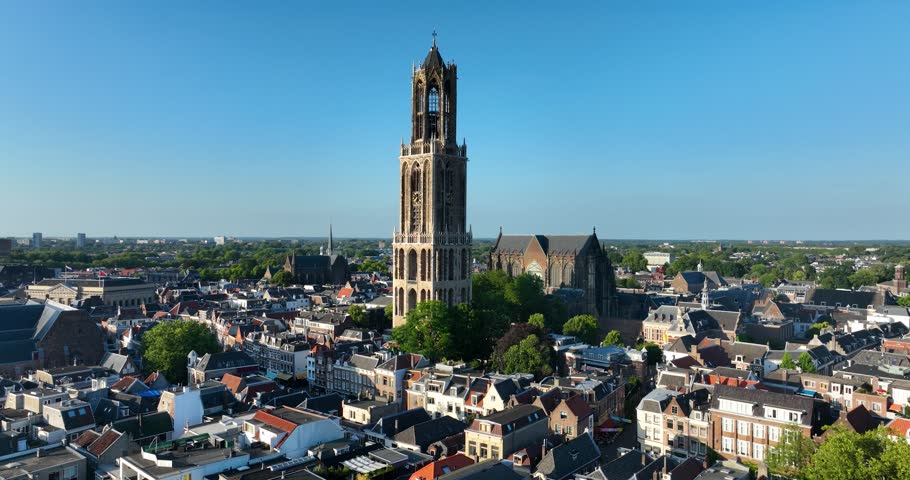 A drone view of the Dom Tower surrounded by urban buildings on a sunny day with clear sky in Utrecht, The Netherlands