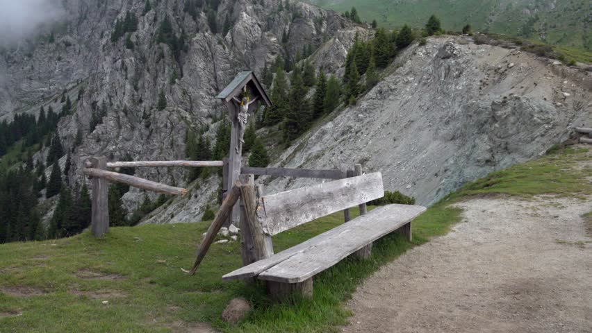 A wooden bench and a cross as a rest area on the hiking path leading to Mount Ifinger, South Tyrol, Italy