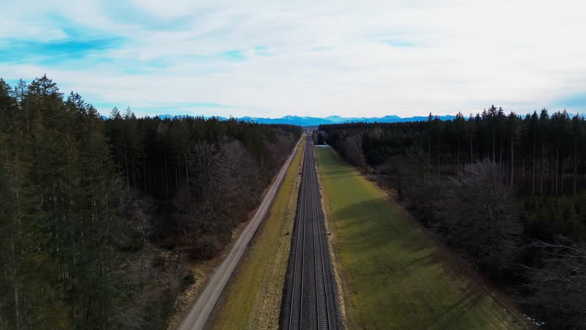 Aerial View of Railway Tracks Stretching Through Dense Forest with Distant Mountain Range