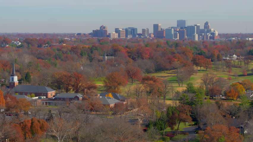 Aerial toward downtown Clayton skyline in St. Louis, Missouri, with a beautiful park in the foreground. Vibrant fall foliage, and urban architecture create a stunning seasonal contrast.