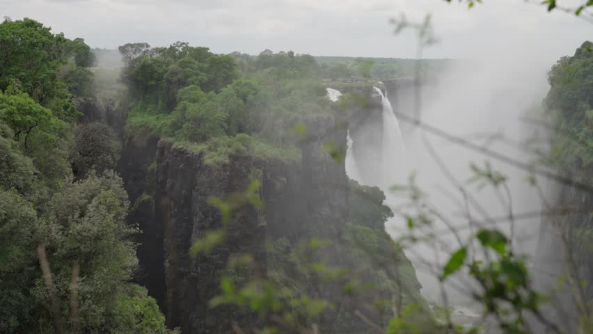 A veil of water falling over cliffs amongst lush green vegetation called Victoria Falls in Zimbabwe