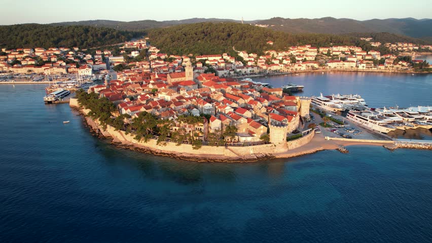 Parallax drone shot of Korcula Old Town and port at sunrise with blue water of the Adriatic Sea in Croatia