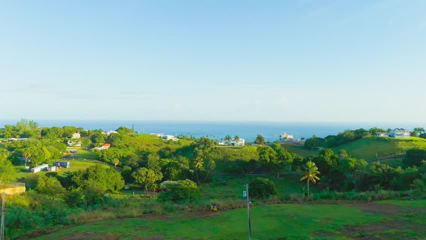 An aerial footage of a small village on a green hill overlooking the ocean on a sunny day in Puntas, Rincon, Puerto Rico