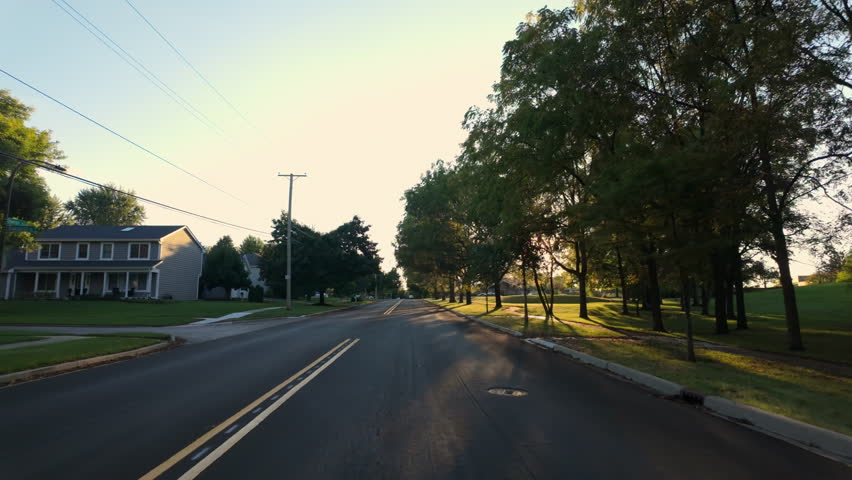 A wide POV shot captures a suburban street in a U.S. residential area on a beautiful sunny day, filmed from a moving car.