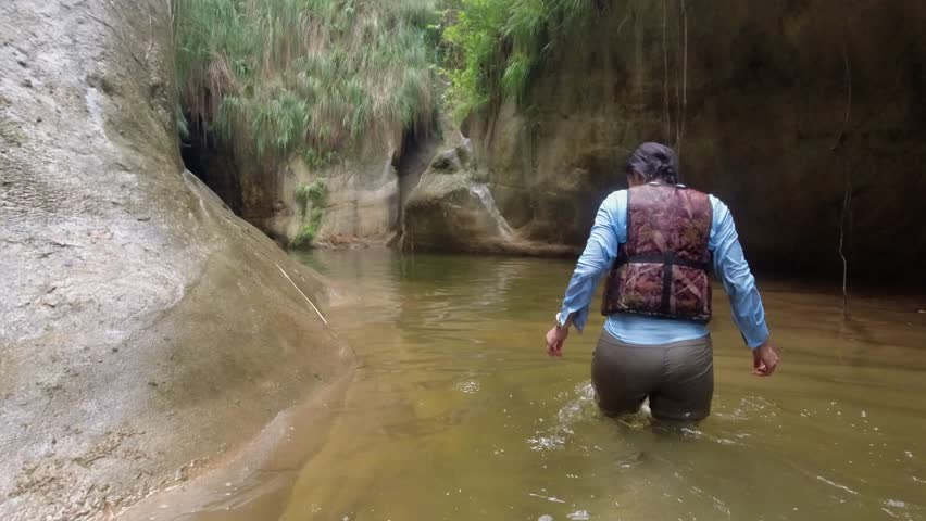 Female canyoneer in narrow canyon river approaches cave resurgence