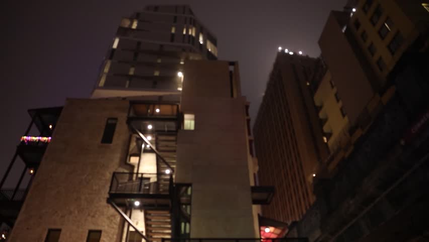 A smooth shot glides past a glowing building, its lights diffused by thick fog, creating an eerie yet mesmerizing nightscape.