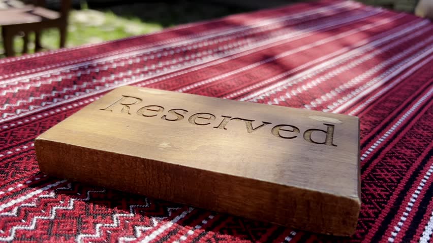 Close-up of a wooden 'Reserved' sign on a red patterned fabric, signifying a special spot or event. The sign's rustic design contrasts with the bright, intricate patterns of the fabric. Reserved Sign