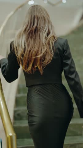 Confident woman in a black suit and sunglasses holding a smartphone in a sleek, modern interior. Ideal for themes of fashion, confidence, and business. Fashionable Young Beautiful Woman. Vertical.