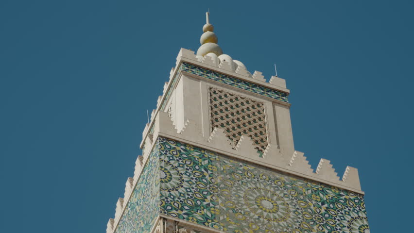 Close-up of Hassan II Mosque's minaret in Casablanca, Morocco, showcasing intricate tilework and ornate architecture on a sunny day. This magnificent landmark offers a glimpse into Moroccan artistry