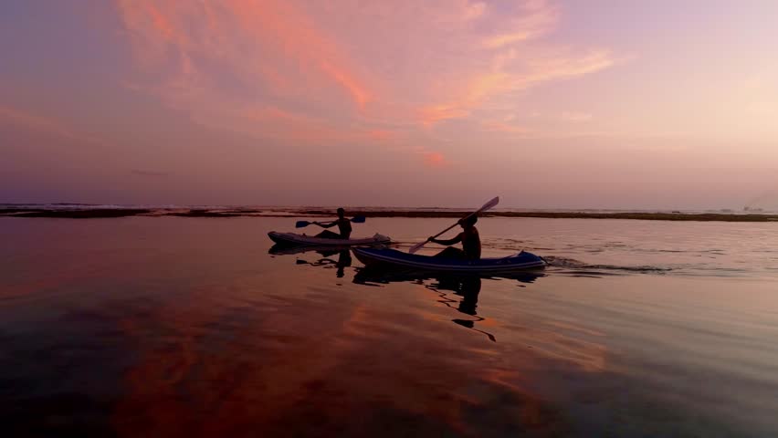 Silhouette Couple friends canoeing on a wooden canoe during a colorful sunny sunset. Cloudy Sky Composite.