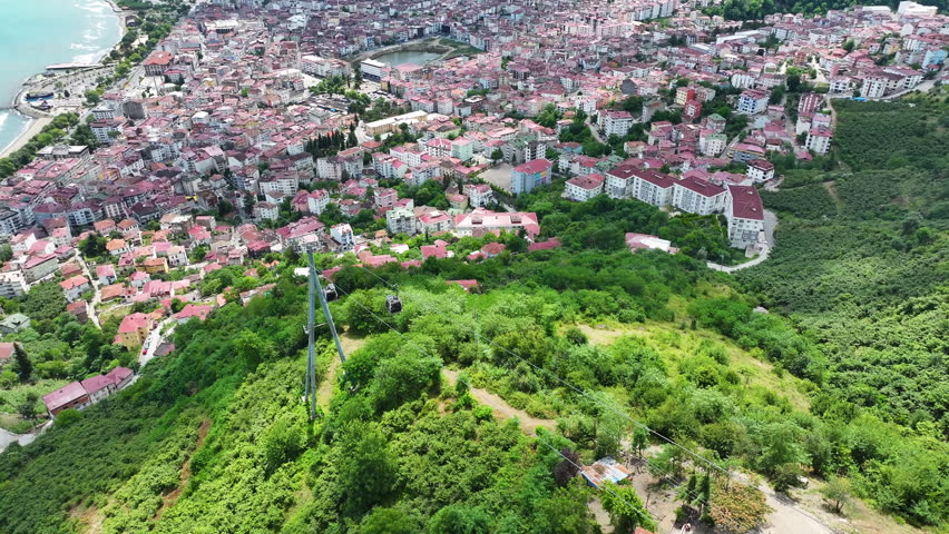 Aerial view of a cable car on a green hill with the city of Ordu and coastline in the background, oe01