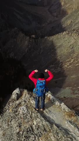 Backpacker with raised arms celebrating reaching mountain peak, enjoying inspiring view of valley and snow-capped peaks of Altai Mountains in autumn