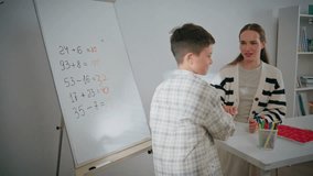 Diligent pupil writing whiteboard at school closeup. Little child boy taking felt-tip-pen solving mathematical equations during lesson. Woman teacher sitting in classroom. Clever kid learning at board - Powered by Shutterstock - Get 15% off with code: PIKWIZARD15