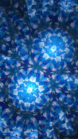 A vertical look into a kaleidoscope showing slow motion of fractals with floral patterns in various blue hues and tints rotating, deepening, scaling and reflecting in the room of mirrors.