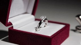 A stunning 4K cinematic close-up shot featuring a small, elegant jewelry box slightly open, revealing a dazzling engagement ring nestled inside, placed against a bold, deep red background. - Powered by Shutterstock - Get 15% off with code: PIKWIZARD15