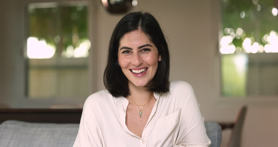 Beautiful young Hispanic brunette woman posing for video call head shot, looking at camera with happy toothy smile, laughing out loud, opening perfect healthy white teeth. Latin female model portrait