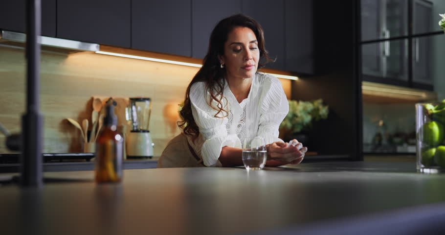 Woman, pill box and drinking water in home, supplements and vitamin b tablets for menopause. Kitchen, container and drugs storage for chronic treatment, medication and omega 3 to remedy condition