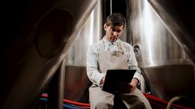 Professional brewer analyzing data and making notes on tablet in front of stainless steel tanks - Powered by Shutterstock - Get 15% off with code: PIKWIZARD15