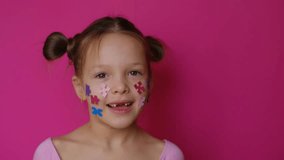  Cute preschool-age girl with cheeks decorated with paper pieces of colorful puzzles. A cheerful child on a pink studio background of bright pink color. - Powered by Shutterstock - Get 15% off with code: PIKWIZARD15