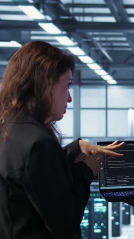 Vertical video Software developers using AI tech on laptop in data center managing server virtualization. IT expert coding on notebook in server room using artificial intelligence, finetuning network