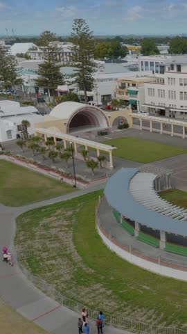Aerial view of a town square with a bandstand and covered seating area. People stroll through the park. Public space for relaxation and entertainment. Napier Soundshell,  Hawkes Bay, New Zealand