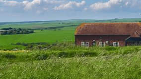 Charming cottage with a rustic roof set amidst the rolling green fields of Eastbourne, East Sussex, United Kingdom. The bright blue sky and fluffy clouds enhance the idyllic countryside setting - Powered by Shutterstock - Get 15% off with code: PIKWIZARD15