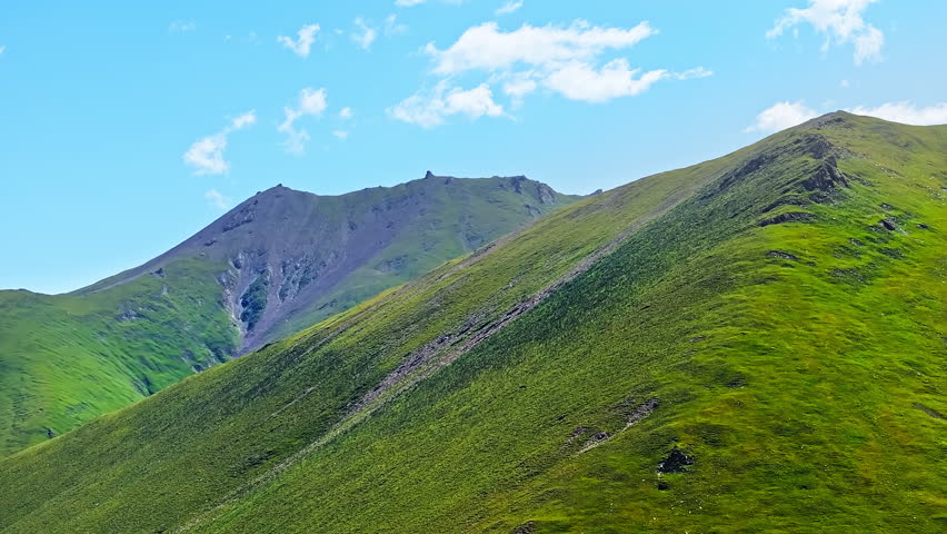 Green grassland and mountain range natural landscape under blue sky. Summer scenery.