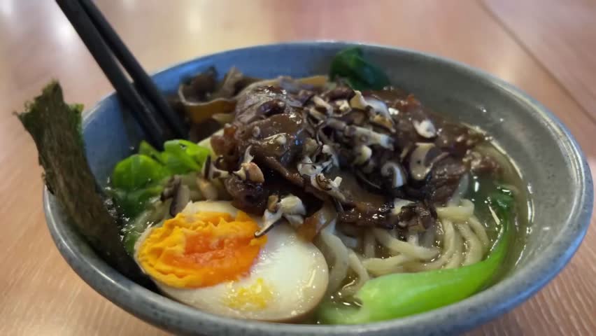 Close up video Deliciously crafted bowl of ramen featuring tender beef, fresh vegetables, boiled egg, and hearty broth. 
