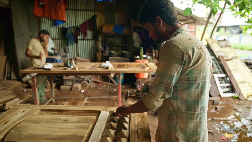 Furniture maker taps nails into the wood using hammer, Carpenter fastens wooden panels to build a sturdy door, Artisan perfects each joint, Woodworker assembling the frame, under rustic shelter, Shop