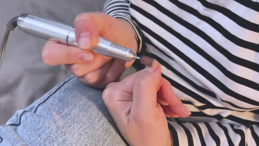 The master does a manicure to his client. A professional manicurist cleans the nails of a young girl with a file